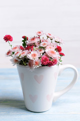Beautiful flowers in cup on table on light background