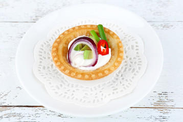Tartlet with greens and vegetables with sauce on plate on table