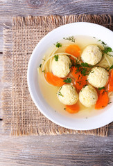 Soup with meatballs and noodles in bowl on wooden background