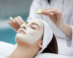 Beautiful young woman receiving facial mask of cucumber in beaut