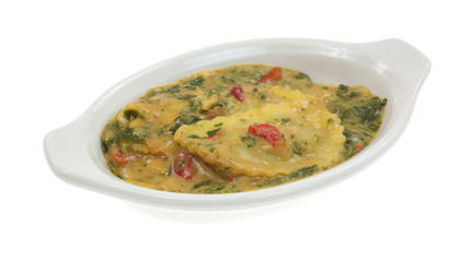 A baking dish with cooked ravioli in wine sauce with spinach