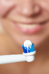 Woman brushing teeth electric toothbrush with toothpaste macro