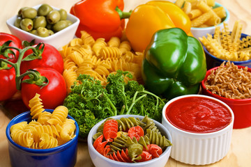 Variety of uncooked italian pasta with vegetables on wooden