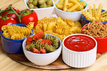 Variety of uncooked italian pasta with vegetables on wooden