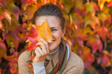 Portrait of happy young woman hiding behind autumn leafs 