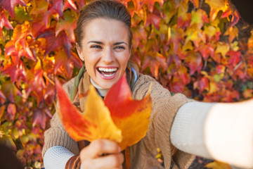 Smiling young woman with autumn leaf making selfie