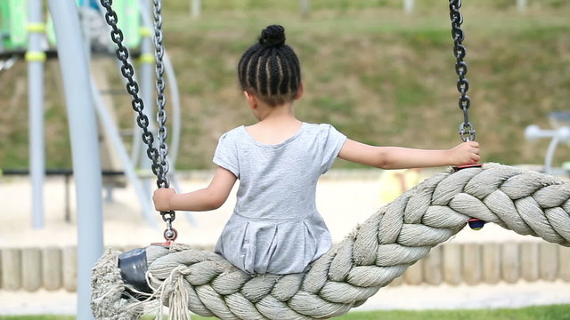 Young girl sits alone on a swing as children play around her
