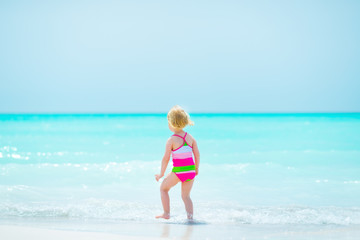 Baby girl standing on sea coast. rear view