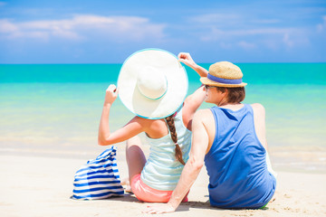 back view of couple in straw hats sitting at tropical beach