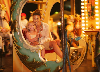 Fototapeta na wymiar Portrait of happy mother and baby girl riding on carousel