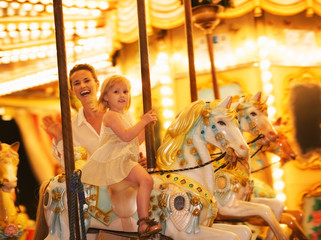 Obraz na płótnie Canvas Portrait of happy mother and baby girl riding on carousel