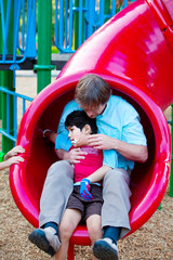 Fototapeta na wymiar Caucasian father helping disabled son down slide at playground