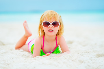 Portrait of baby girl in sunglasses laying on beach