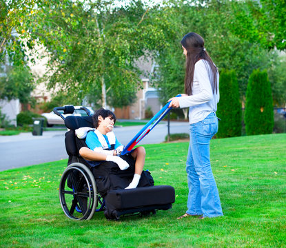 Biracial older sister playing outdoors with disabled little brot