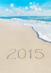 inscription 2015 on sea sand beach with the sun rays against wav