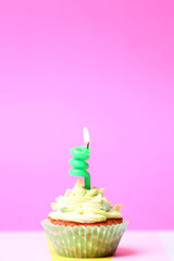 Delicious birthday cupcake on table on pink background