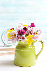 Beautiful flowers in pitcher on table on light blue background
