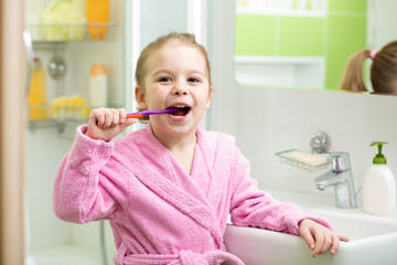 Smiling little girl brushing teeth in bathroom