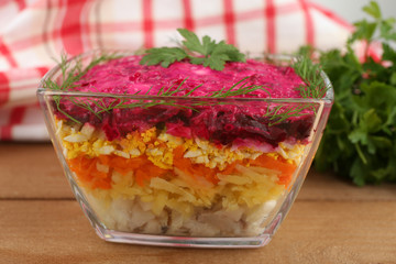 Russian herring salad in glass bowl on wooden table background