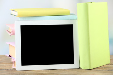 PC tablet and books on wooden table, on light background