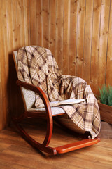 Rocking chair with plaid near wooden wall