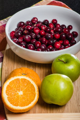 Bowl of cranberries with apples and oranges on board