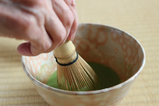 畳の上で萩焼の茶碗を使い茶筅で抹茶を点てる女性の手元クローズアップ