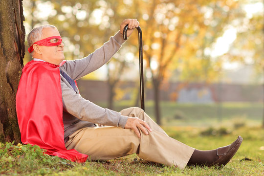 Senile Old Man Sitting Outdoor In Superhero Costume