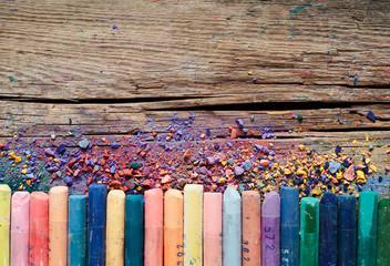 Pastel crayons and pigment dust on rustic wooden background.