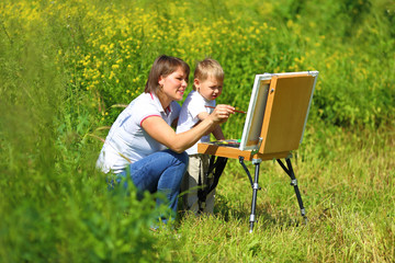 Mom and baby paint on an easel in the field