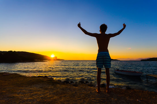 man at sunset standing with arms raised up above