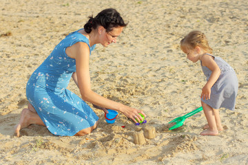 Mom with a baby girl playing in the sand on the beach