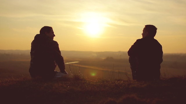 The two friends sit by sunset (sunrise) background on the hill
