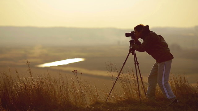 The photographer works near the tripod by sunset background