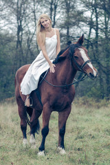Fototapeta premium romantic sensual girl in white dress on a horse in the forest