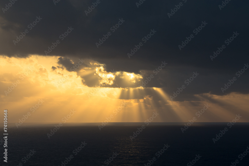 Wall mural Dramatic sunset rays through a cloudy dark sky over the ocean