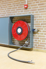 Red fire hose on reel at wall