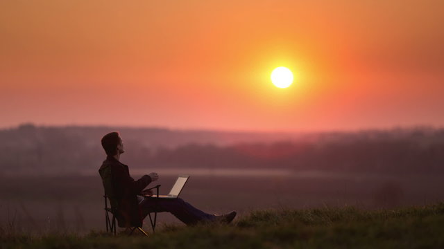 Man with PC at the hill top, sunset time lapse