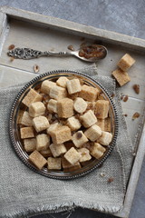 Heap of brown sugar cubes on metal plate on wooden tray