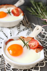 Fried egg with bacon in ceramic pan on wooden background