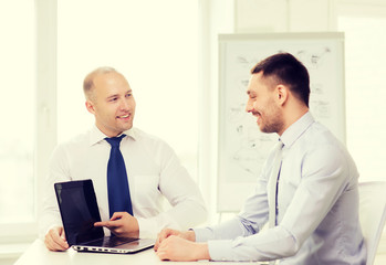 Obraz premium two smiling businessmen with laptop in office