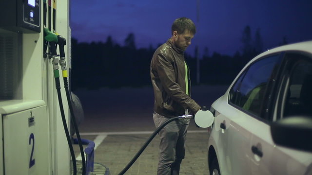 Filling station. A man fills his car with gasoline at night