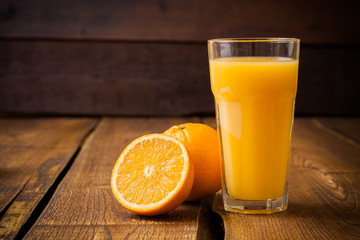 Orange fruit and glass of juice on brown wooden background