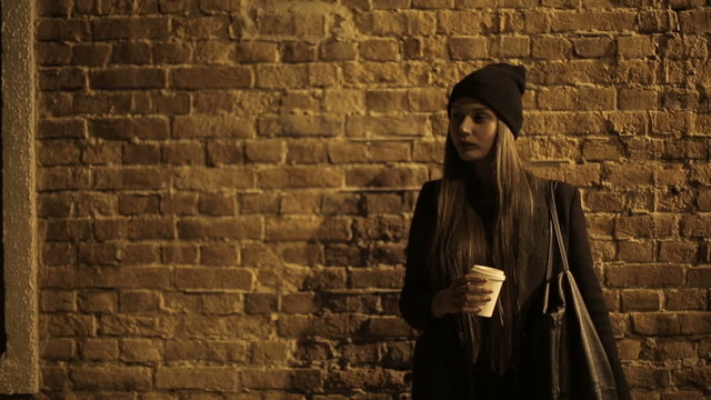 Girl teenager in the street at night drinking coffee and waiting