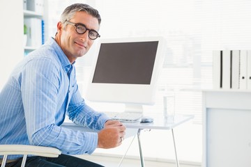 Smiling man with glasses at his desk looking at camera