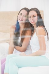 Obraz na płótnie Canvas Pretty friends smiling at camera on bed