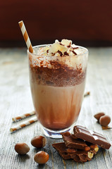 Chocolate smoothie in glass on wooden background with straw