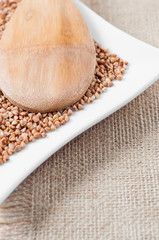 Spoon with buckwheat on white background and burlap