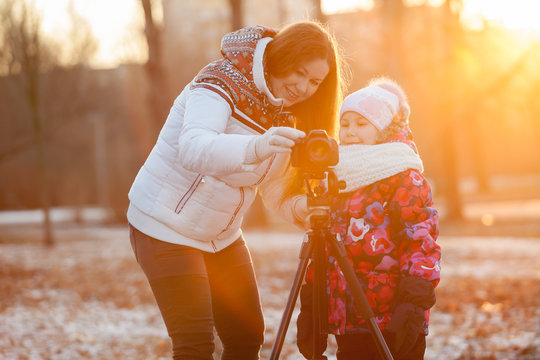 Mother and child set up camera on tripod in rays of setting sun