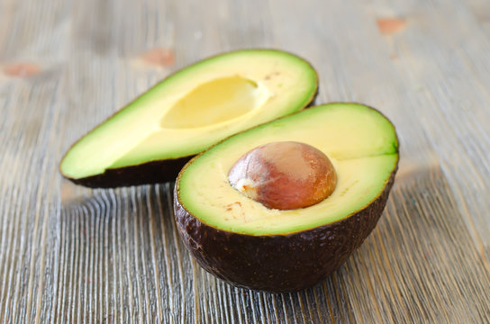 Avocado cut in halves with stone on wooden table